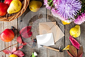 Thanksgiving background with seasonal fruits, flowers, greeting card and envelope on a rustic wooden table. Autumn harvest concept