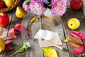 Thanksgiving background with seasonal fruits, flowers, greeting card and envelope on a rustic wooden table. Autumn harvest concept