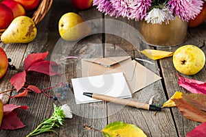 Thanksgiving background with seasonal fruits, flowers, greeting card and few craft envelopes on a rustic wooden table. Autumn harv