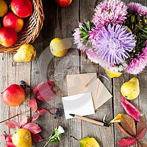 Thanksgiving background with seasonal fruits, flowers, greeting card, few craft envelopes on a rustic wooden table. Autumn harvest