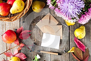 Thanksgiving background with seasonal fruits, flowers, greeting card, few craft envelopes on a rustic wooden table. Autumn harvest