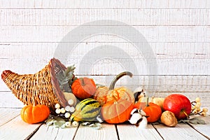 Thanksgiving cornucopia filled with autumn vegetables and pumpkins against white wood