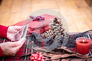 Thanksgiving day. Wooden table with red accessories, gift, candle and flowers. Human hands of woman using tablet and technology