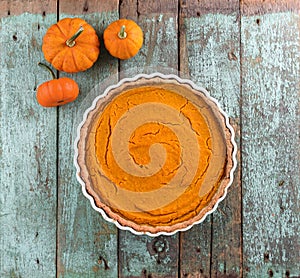 Thanksgiving dessert. Homemade rustic open pumpkin pie with small decorative pumpkins on shabby blue wooden table