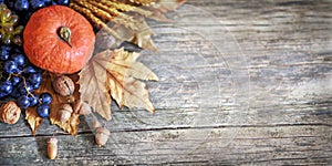 Thanksgiving dinner background with autumn orange pumpkin, seasonal fruit crop and maple leaves on vintage wooden table.