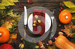 Thanksgiving dinner place setting. Autumn fruit, pumpkins, nuts, fallen leaves with plate and cutlery. Thanksgiving autumn