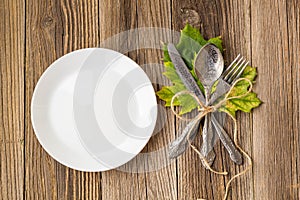 Thanksgiving dinner plate with fork, knife and autumn leaves on rustic wooden table background. Top view, copy space