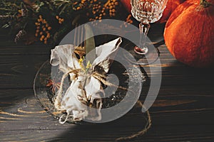 Thanksgiving dinner table setting. Modern plate with vintage cutlery, linen napkin, herb and glass on wooden table with pumpkins
