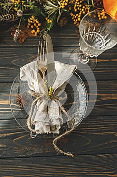 Thanksgiving dinner table setting. Stylish plate with cutlery and autumn decorations, pumpkin, natural branches and autumnal