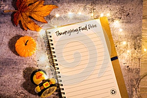 Thanksgiving Food Drive list concept on notebook surrounded with bright leaves and decorative lights, flat lay