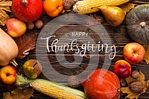 Thanksgiving greetings. Pumpkins, vegetables, nuts, dry leaves on a wooden background, top view. Kaligraphic capital inscription