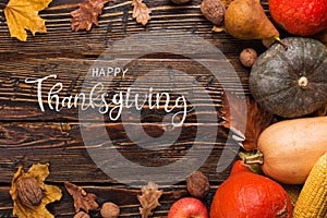 Thanksgiving greetings. Pumpkins, vegetables, nuts, dry leaves on a wooden background, top view. Kaligraphic capital inscription