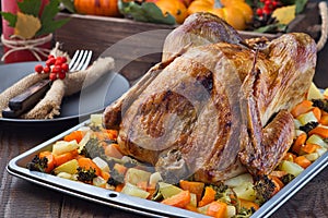 Thanksgiving roasted turkey with vegetables, carrot, parsnip, potato on a tray. Autumn decorations with leaves, rowan berries and