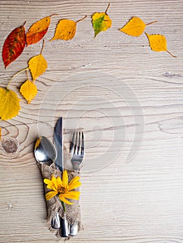 Thanksgiving table setting cutlery on the autumn background with autumn leaves,yellow flower on wooden surface