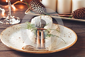 Thanksgiving table setting among white candles and cones. Ceramic plate with fork and knife on a linen napkin