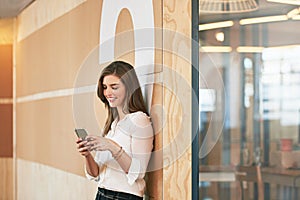 Thats a great text to start the day. a smiling young woman using her cellphone while standing in an office.