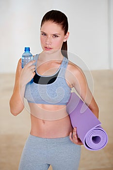 Thats refreshing. Portrait of an attractive young woman holding a bottle of water and an exercise mat.
