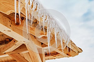 Thawing icicles with water drops falling against blue skies on the wooden roof. Spring is comming.