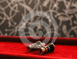 Theatrical metal binoculars lies on red velvet against a blurred stage of a theater curtain