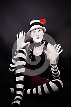 Theatrical mime with red flower sits on the floor