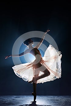 Theatrical performance. Beautiful, tender, graceful ballerina dancing against dark blue background with spotlight