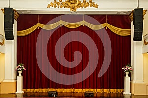 Theatrical stage curtain red heavy velvet with gold fringe flowers in vases at the corners.