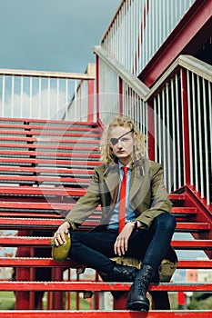 A theatrically dressed pseudo soldier or pirate with a blindfold in one eye sits on the stairs. Young man with a viking haircut