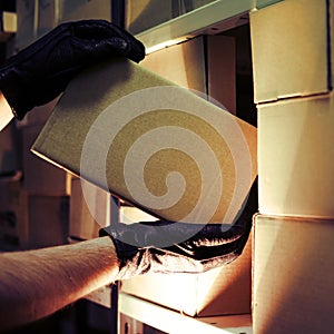 Theft of a box with a parcel in a warehouse. Man hands in gloves steal a box in a warehouse at night