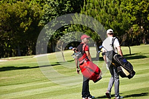 On their way to the next hole. two men carrying their golf bags across a golf course.