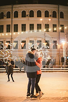 The theme is active recreation in winter on the ice arena. Young caucasian couple happy and in love glide together on an ice rink