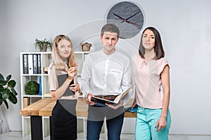 Theme business, teamwork and partnerships. A group of young people, three people, stand in an office near the table in