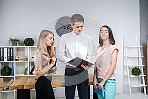 Theme business, teamwork and partnerships. A group of young people, three people, stand in an office near the table in