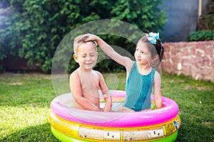 Theme is a children`s summer vacation. Two Caucasian children, brother and sister, sit in a perched round pool with water in the