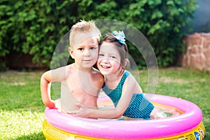 Theme is a children`s summer vacation. Two Caucasian children, brother and sister, sit in a perched round pool with water in the