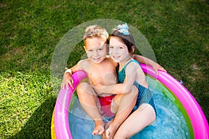 Theme is a children`s summer vacation. Two Caucasian children, brother and sister, sit in a perched round pool with water in the