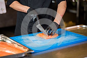 Theme cooking is a profession of cooking. Close-up of a Caucasian man`s hand in a restaurant kitchen preparing red fish fillets