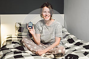 Theme diabetes. young caucasian woman at home in the bedroom on the bed uses the technology of the device for measuring blood