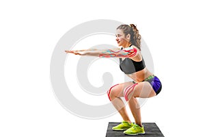 Theme kinesiology tape rehabilitation and health of athletes. Beautiful girl doing a squat exercise on a black rug on a white isol