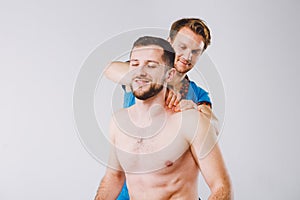 Theme massage and body care. A handsome Caucasian male doctor in blue uniform and beard diagnosing muscles of neck and shoulders,