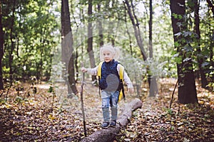 Theme outdoor activities in nature. Funny little Caucasian blonde girl walks walks hiking in the forest on rough terrain with a