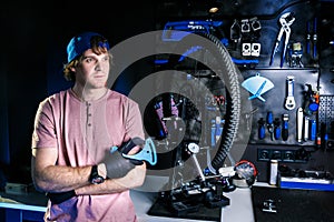 Theme a small business of bicycle repair. stylish man owner of workshop stands near the machine for repairing wheel on background