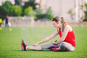 Theme sport and health. Young beautiful Caucasian woman sitting doing warm-up, warming up muscles, stretching green grass.