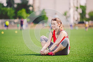 Theme sport and health. Young beautiful Caucasian woman sitting doing warm-up, warming up muscles, stretching green grass.