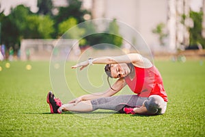 Theme sport and health. Young beautiful Caucasian woman sitting doing warm-up, warming up muscles, stretching green grass.