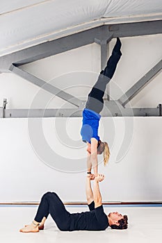 Theme is sports and acreage. A young Caucasian male and female couple practicing acrobatic yoga in a white gym on mats. a man lies