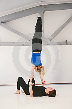 Theme is sports and acreage. A young Caucasian male and female couple practicing acrobatic yoga in a white gym on mats. a man lies