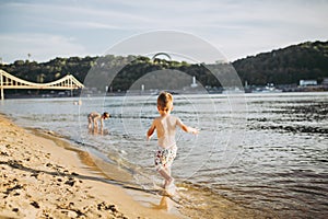 Theme summer outdoor activities near the river on the city beach in Kiev Ukraine. Little funny baby boy running along the river photo