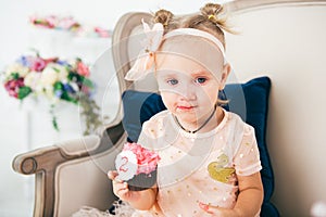 The theme is a sweet dessert cake with the symbol number two 2 for a child`s birthday. A little baby girl sits inside on a chair