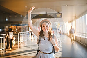 Theme tourism and travel. Young beautiful Caucasian woman in a dress and a hat with a backpack. Tourist mat in the terminal