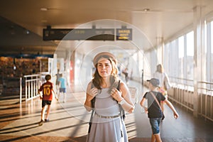 Theme tourism travel. Young beautiful Caucasian woman in dress and hat with backpack tourist mat in terminal station in a long